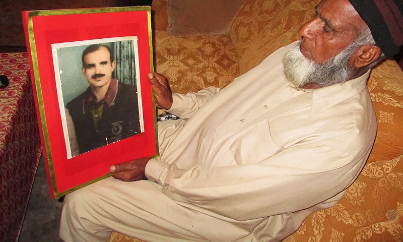 An elderly man holding a framed portrait of Abdul Khaliq